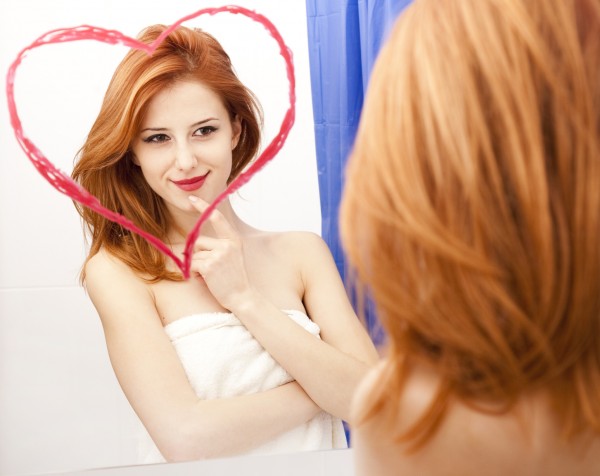 Redhead girl near mirror with heart at it in bathroom.